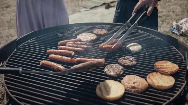 Hand turning sausages and burgers on an outdoor grill